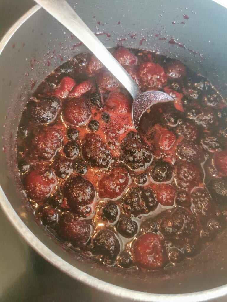 frozen mixed cherries and berries with a spoon simmering in a saucepan.