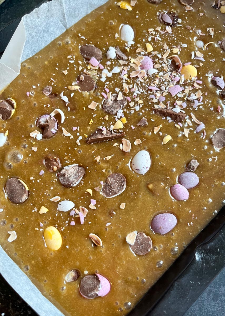 An unbaked blondie topped with mini coloured chocolate eggs in a metal baking tin.