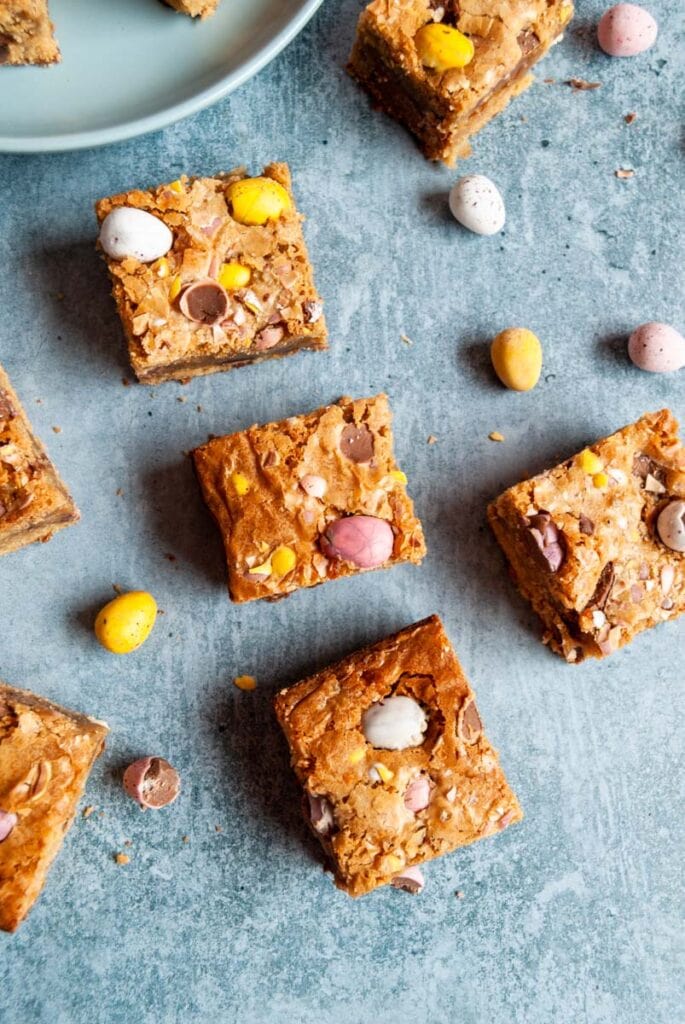 mini egg blondie bars with coloured mini chocolate eggs on a blue backdrop.