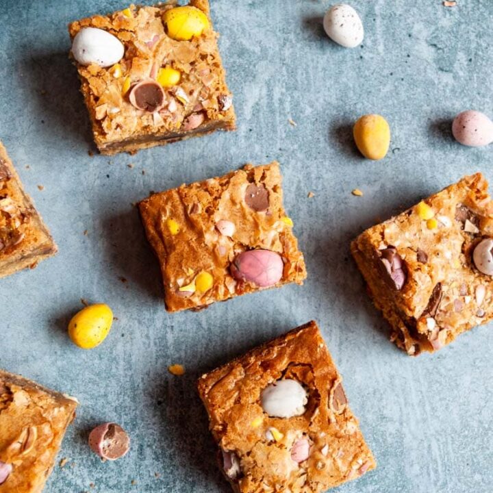 mini egg blondie bars with coloured mini chocolate eggs on a blue backdrop.