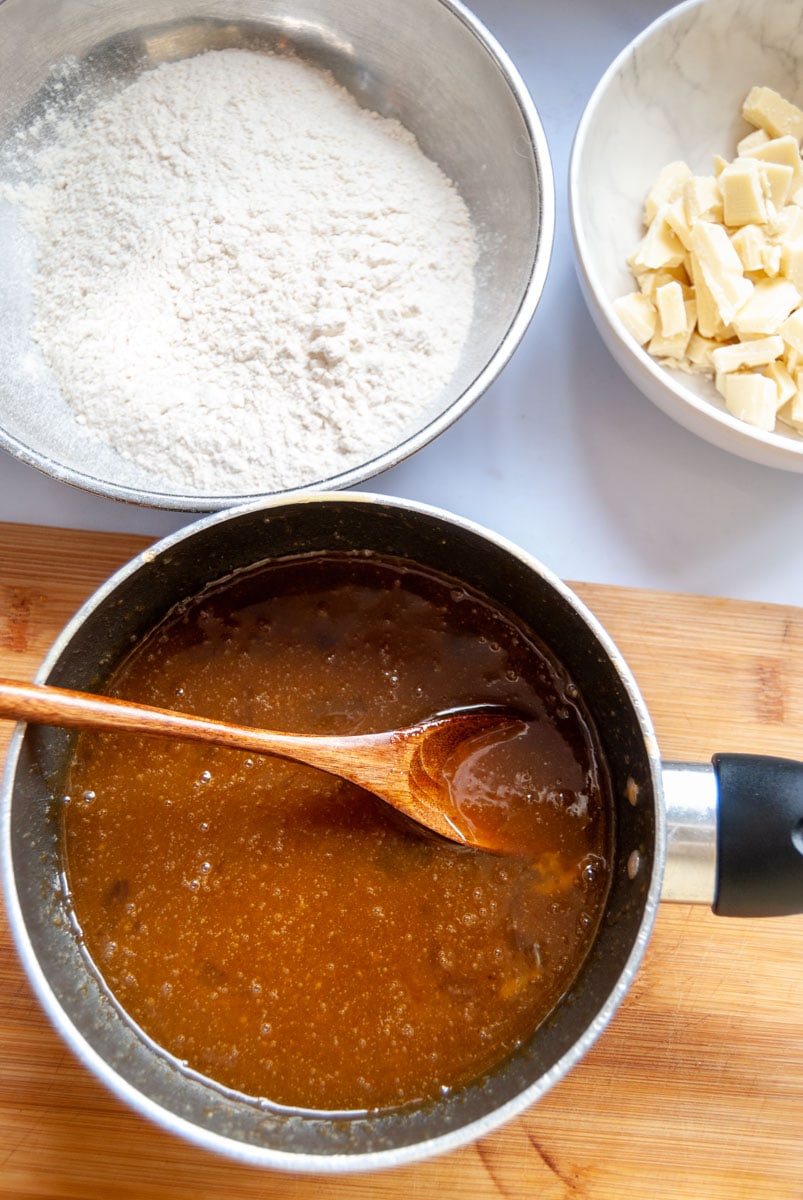 a saucepan of melted butter and brown sugar, a silver bowl of flour and a white bowl of chopped white chocolate.
