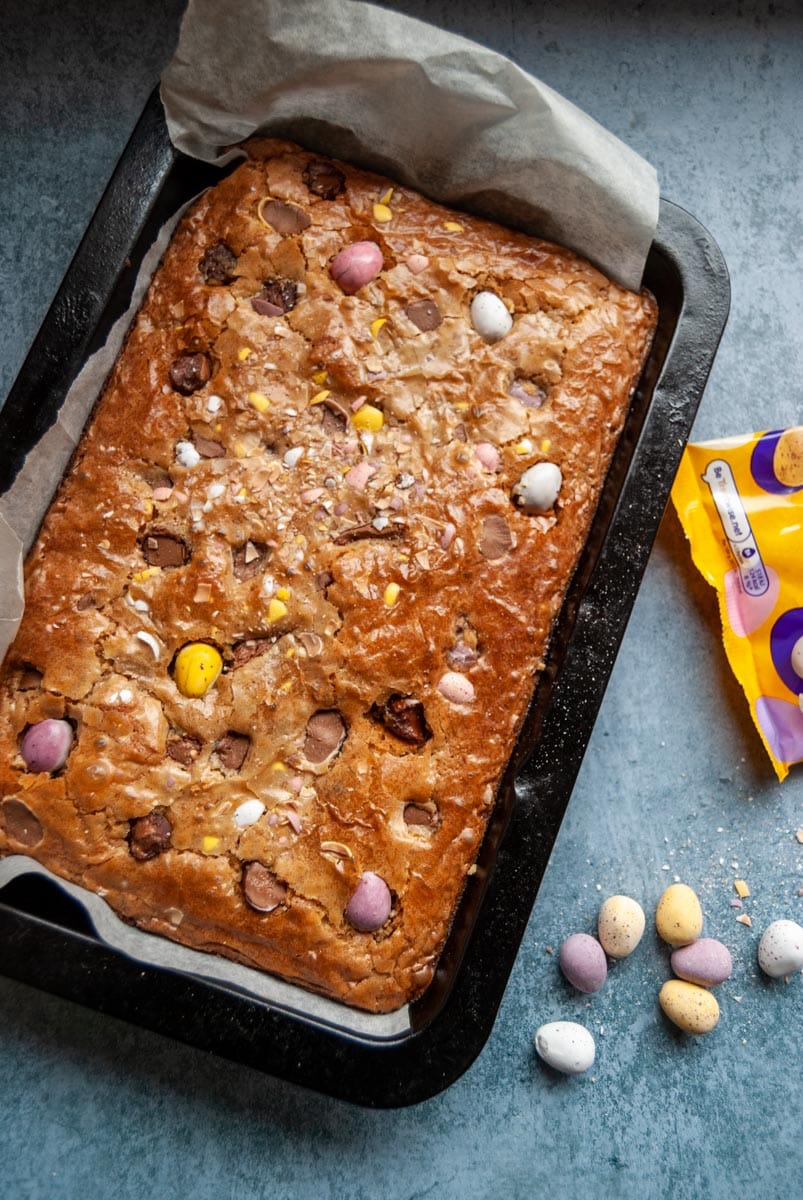 a tray of blondies topped with mini coloured chocolate eggs in a baking tin.