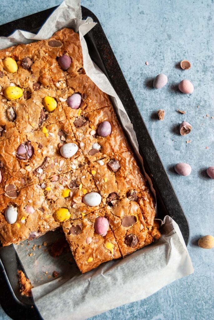 blondies topped with coloured mini chocolate eggs in a lined baking tin.