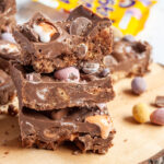 three slices of chocolate fridge cake stacked on top of each other with mini creme eggs and pastel coloured chocolate mini eggs sitting on a wooden board.