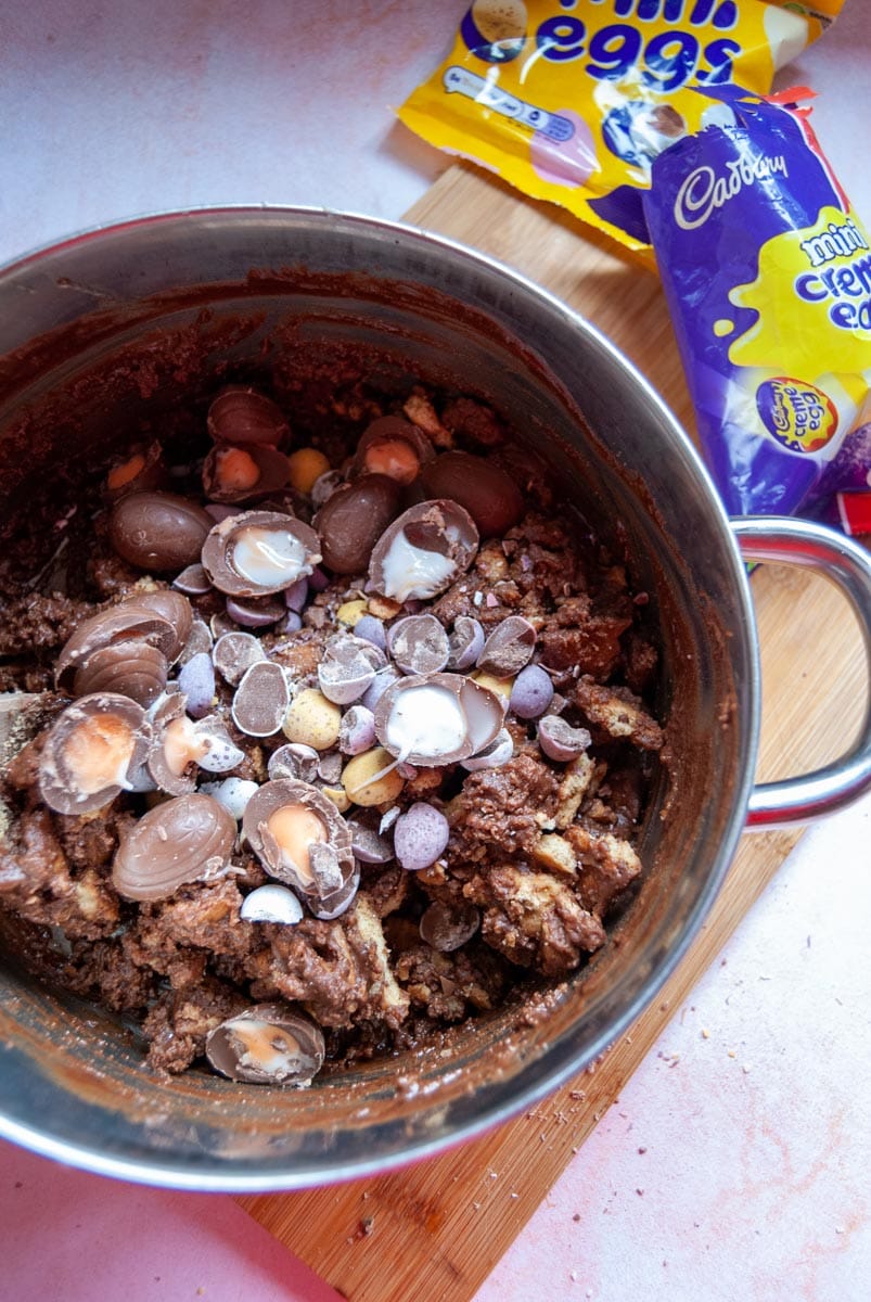 a silver pan of melted chocoalate, crushed biscuits and mini eggs and creme eggs for making fridge cake.
