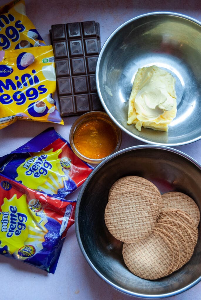 a silver bowl of digestive biscuits, a silver bowl of butter, bars of chocolate, a bowl of golden syrup and packets of Cadbury creme eggs and mini eggs.