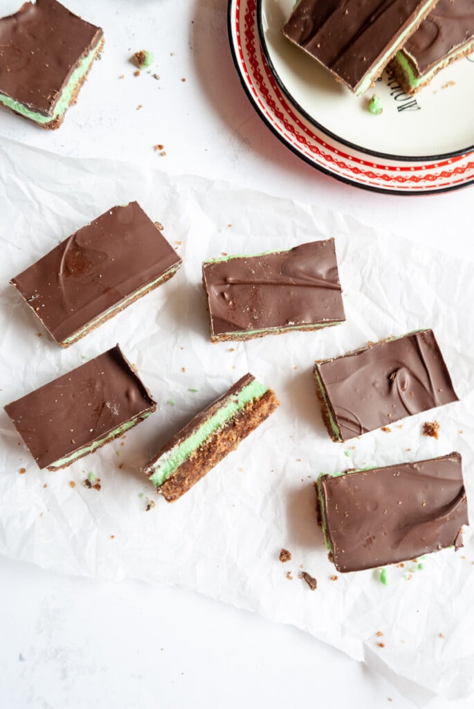 five squares of peppermint bars topped with chocolate on a piece of baking paper.