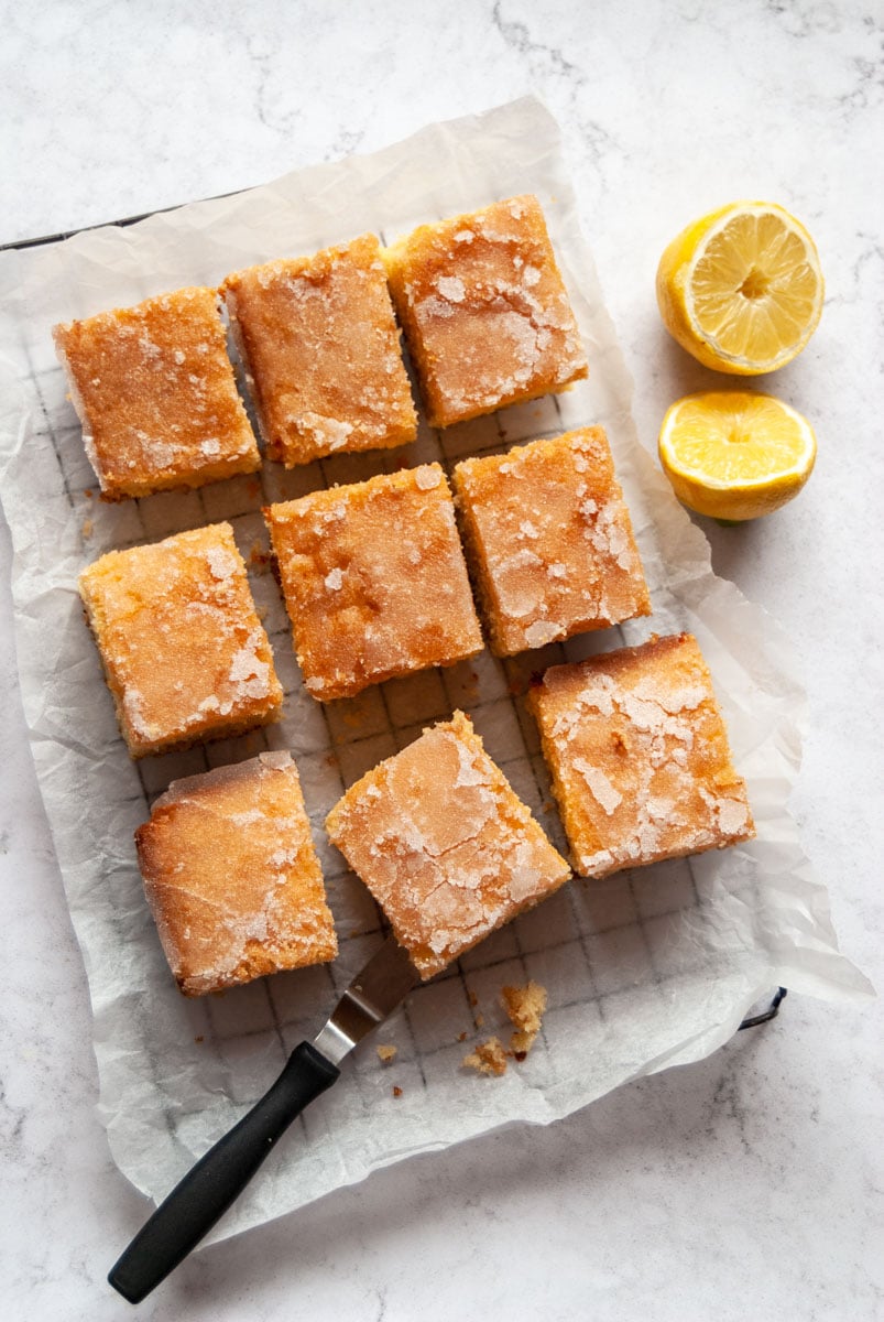 squares of lemon drizzle cake on a wire cooling rack and a halved lemon.