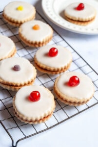 eight Empire biscuits topped with icing and a glace cherry or coloured sweet on a wire cooling rack.