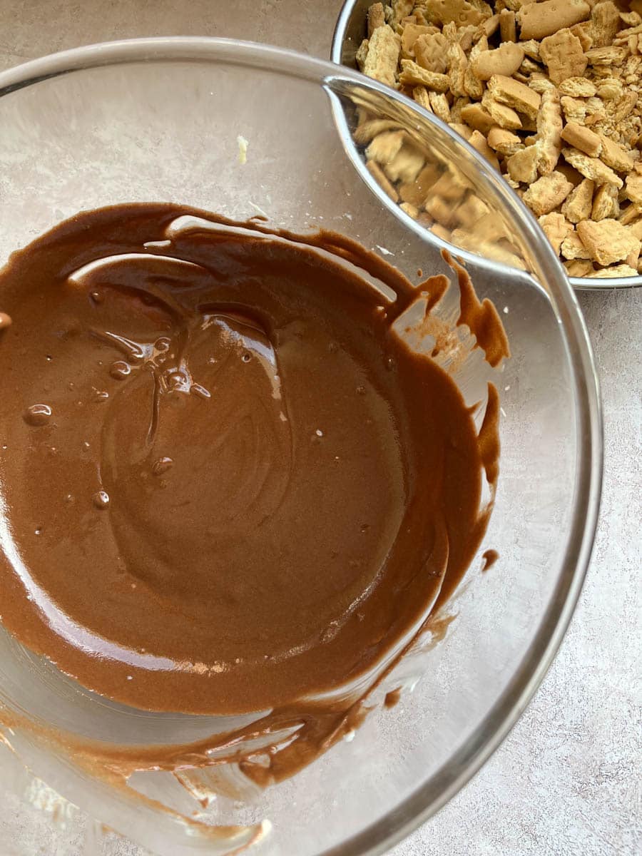 a large mixing bowl of melted chocolate and a silver bowl of crushed biscuits.