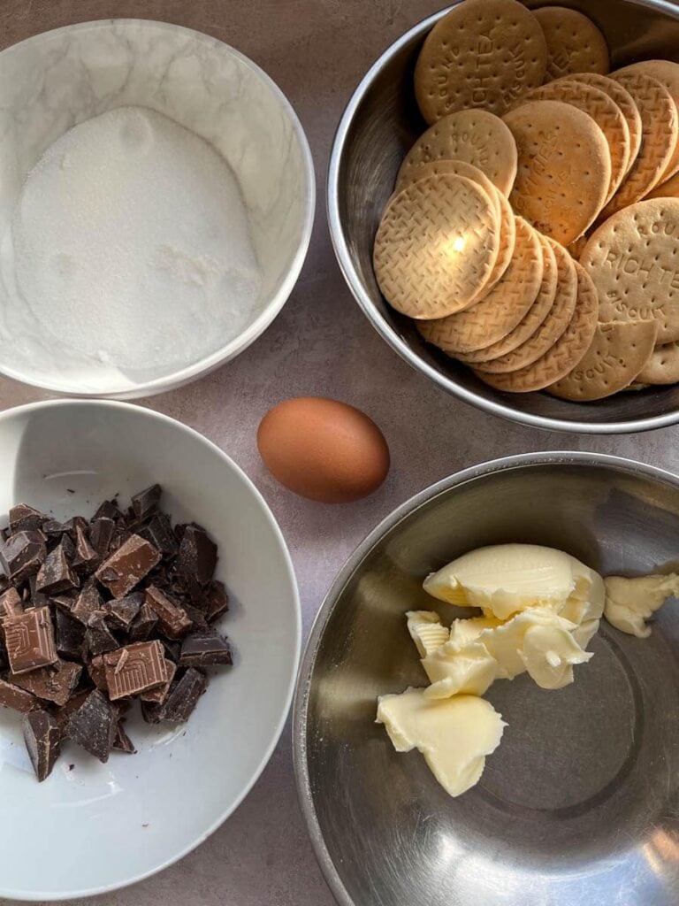 various bowls filled with sugar, butter, rich tea biscuits, chopped chocolate and an egg.