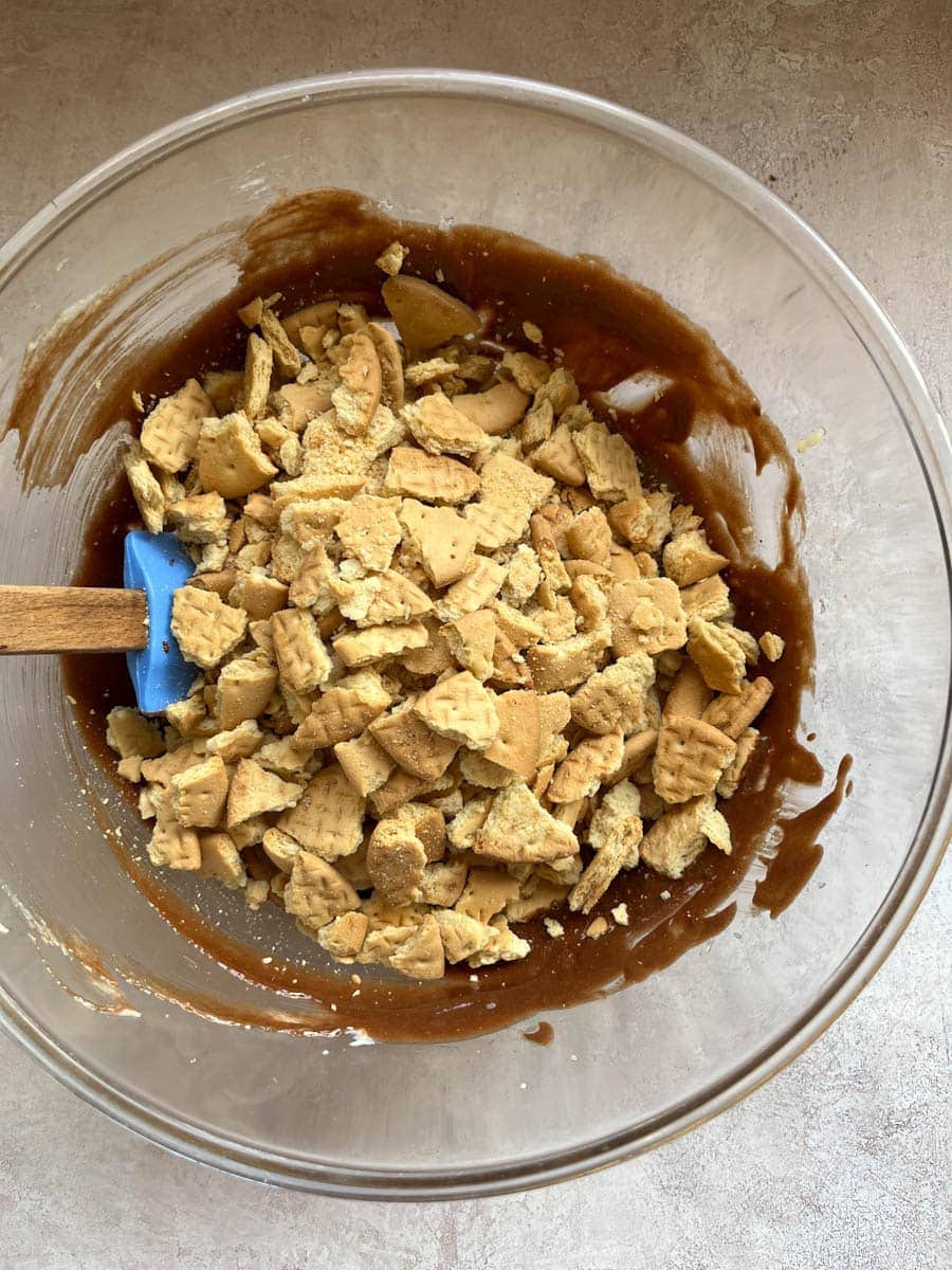 crushed rich tea biscuits being stirred into a large bowl of melted chocolate.