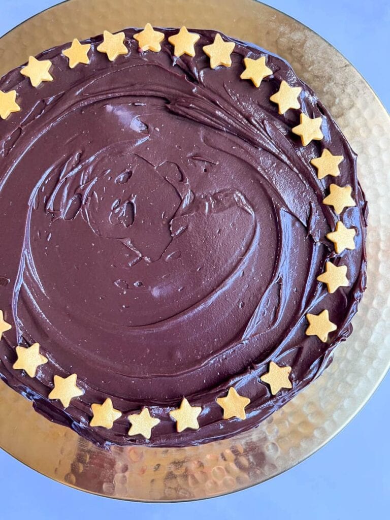 a large round no bake chocolate cake decorated with gold stars on a gold cake stand.