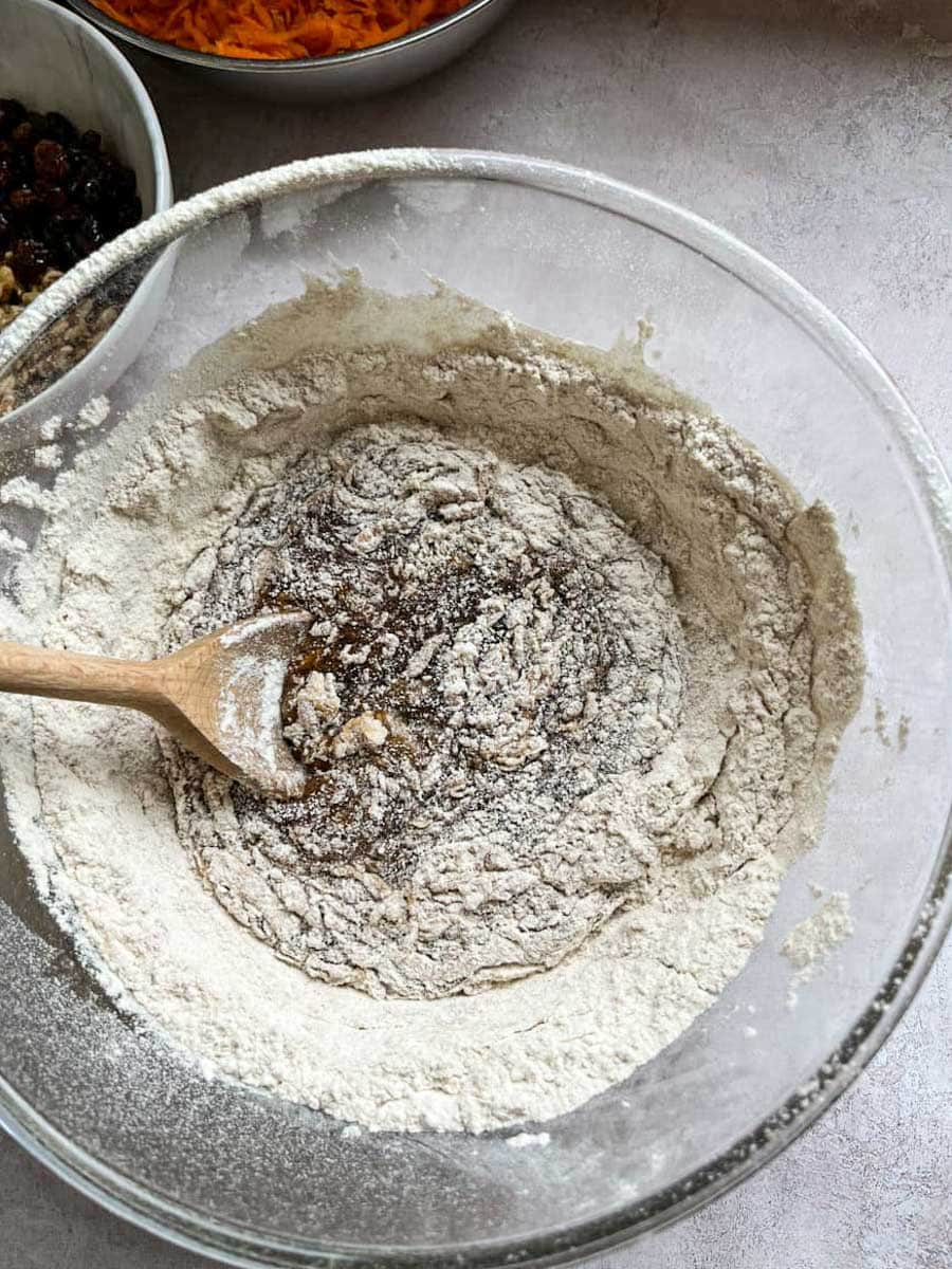 flour being stirred into a bowl of flour, oil, sugar and eggs.