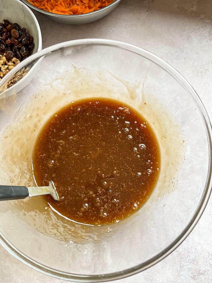 a glass mixing bowl of brown sugar, oil and eggs with a black handled fork.