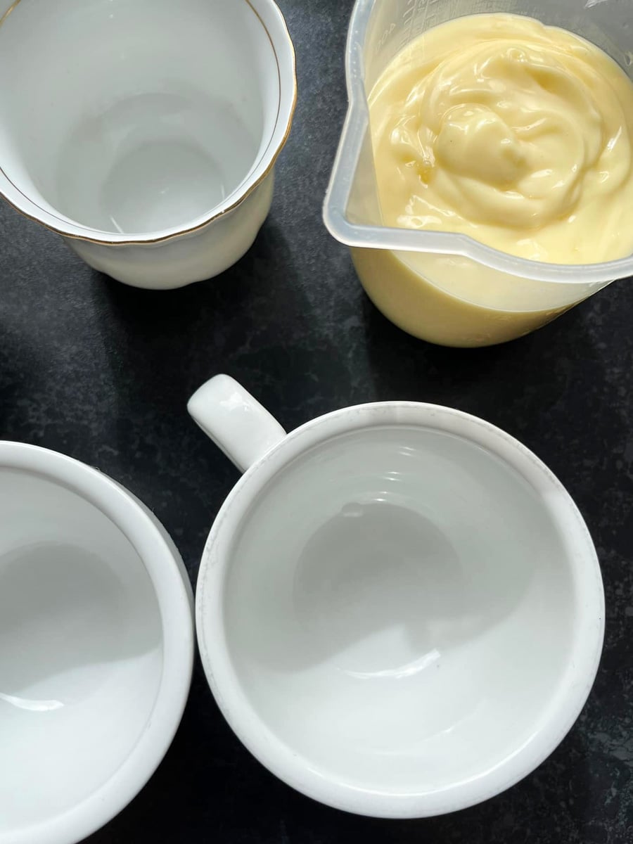 three white teacups and a plastic jug of lemon posset.