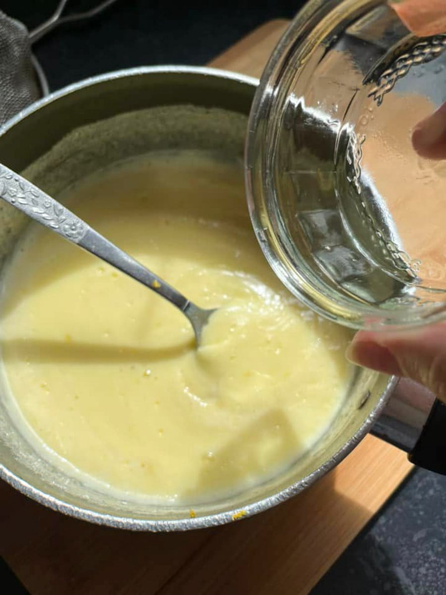 lemon juice being poured from a ramekin into a saucepan of boiled cream and sugar.