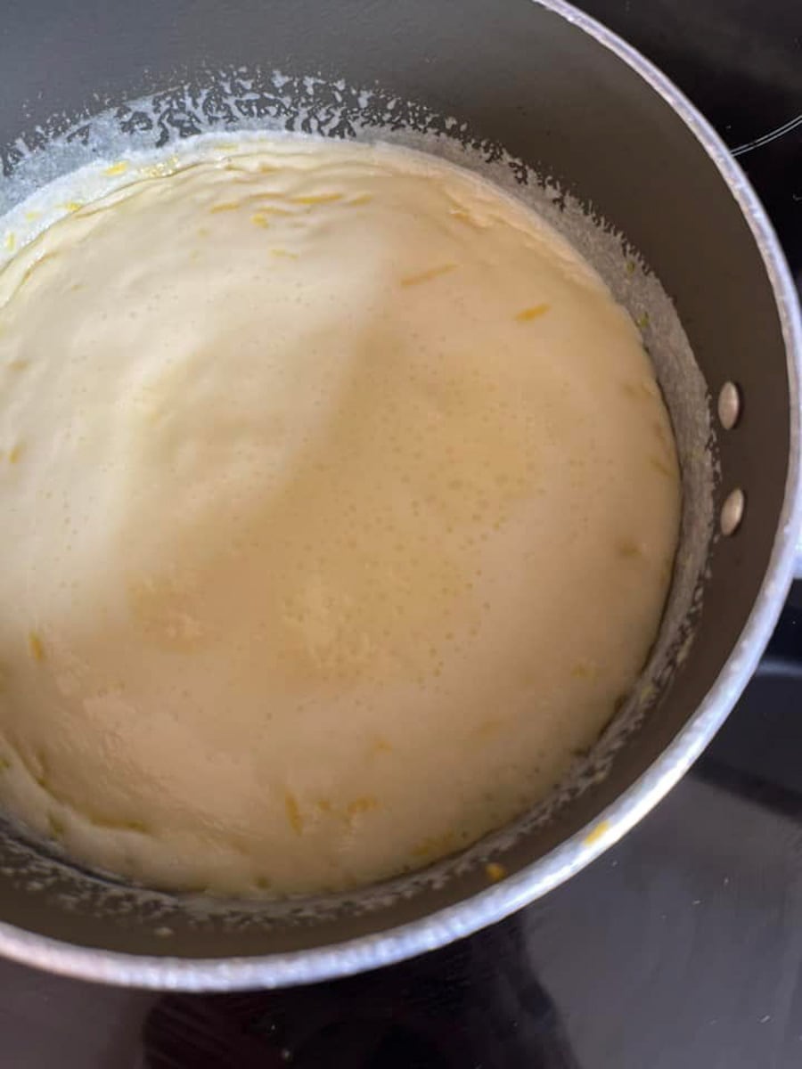 a mixture of cream, sugar and lemon zest boiling in a saucepan on a stove.