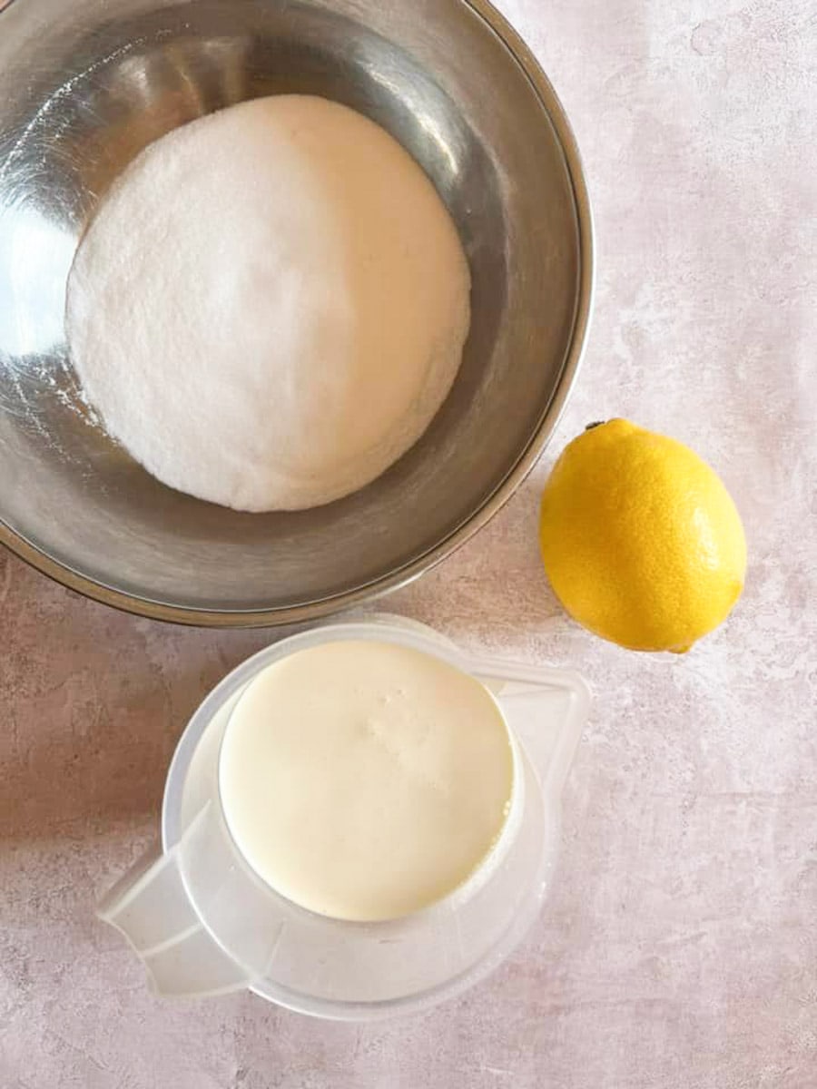 a jug of double cream, a silver bowl of sugar and a lemon on a mottled grey background.