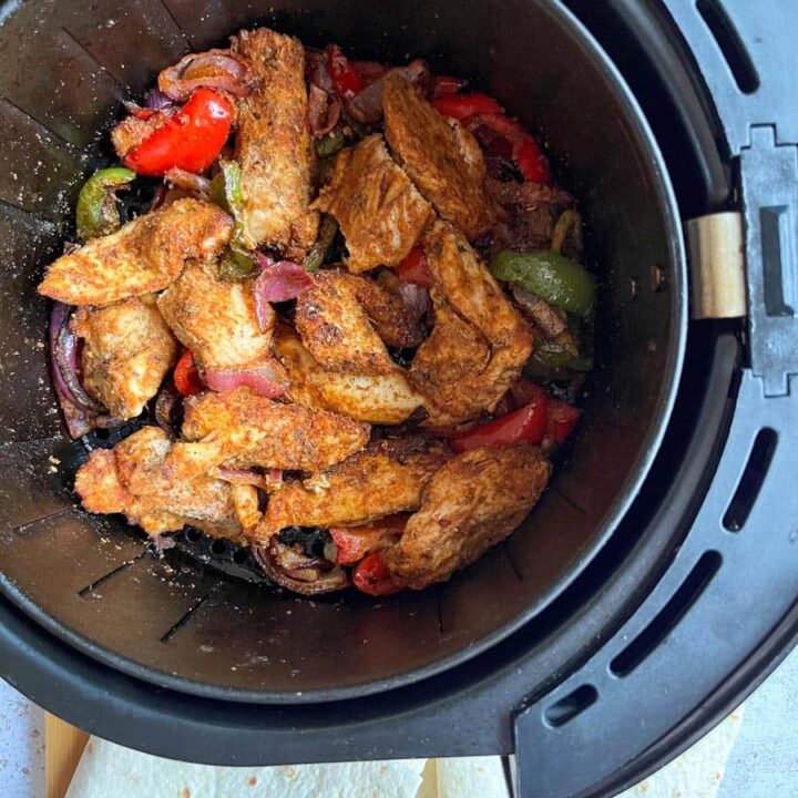 Cooked chicken strips, sliced red onion and green and red bell peppers coated in a fajita spice mix in an air fyer.