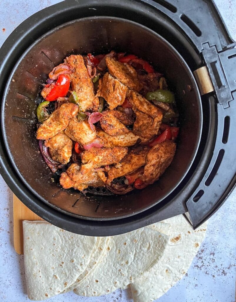 Cooked chicken strips, sliced red onion and green and red bell peppers coated in a fajita spice mix in an air fyer.