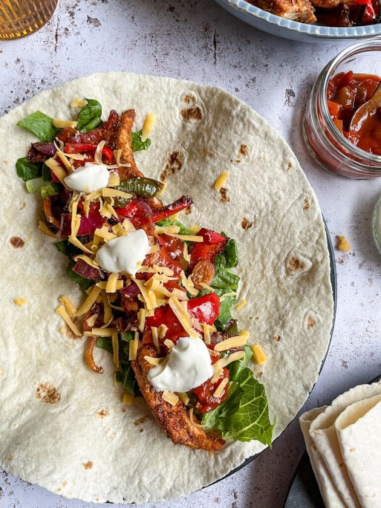 a flour tortilla filled with spiced chicken strips, shredded lettuce, onions, peppers, grated cheese, salsa and sour cream.
