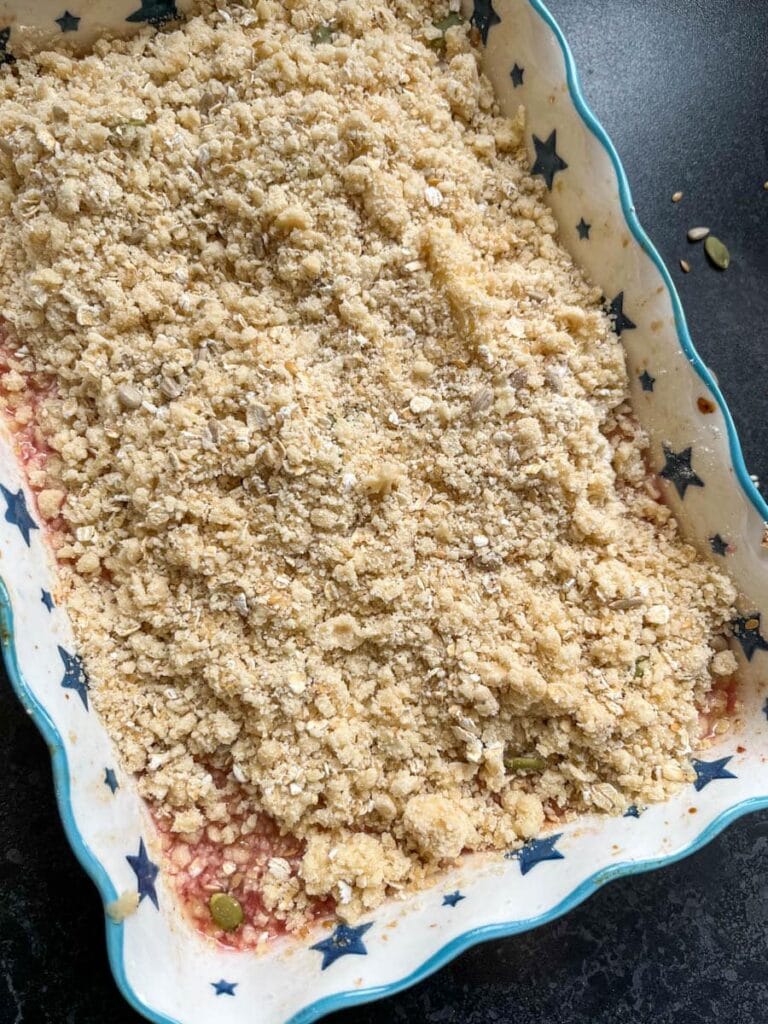 an unbaked plum crumble in a blue and white star patterned baking dish.