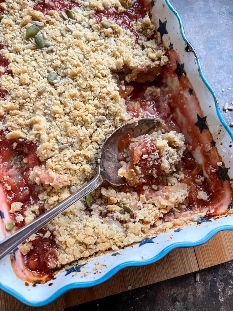 baked plums in a blue and white star patterned dish with an oat crumble with a large silver spoon.