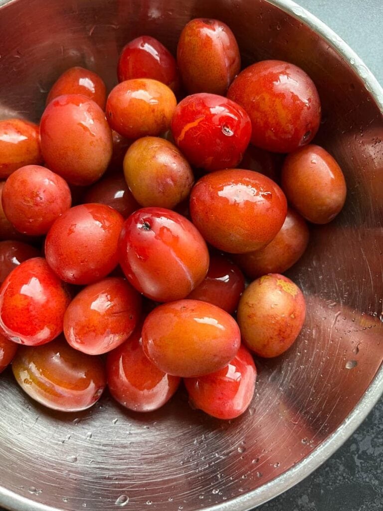 a silver bowl of small red plums.