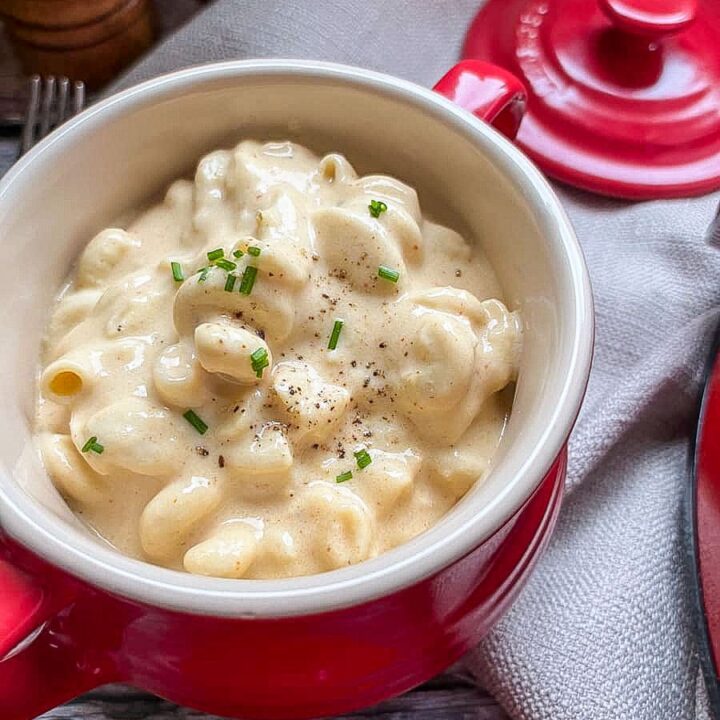 a red and cream bowl filled with macaroni cheese sprinkled with black pepper and fresh chives.