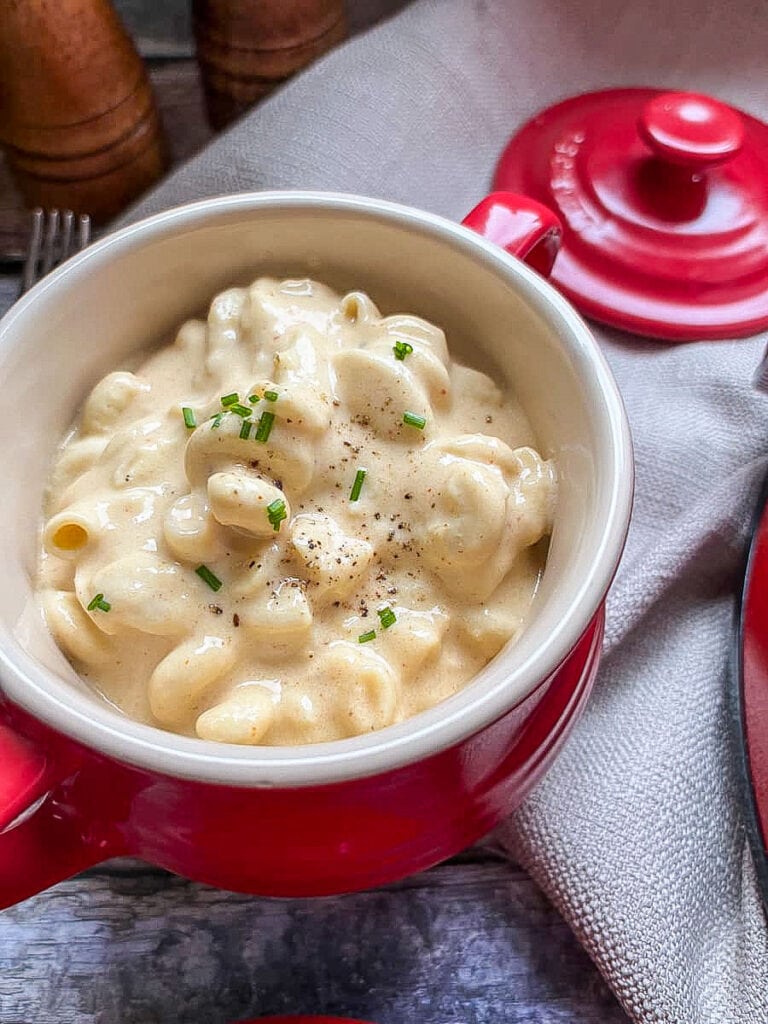 a red and cream bowl filled with macaroni cheese sprinkled with black pepper and fresh chives.