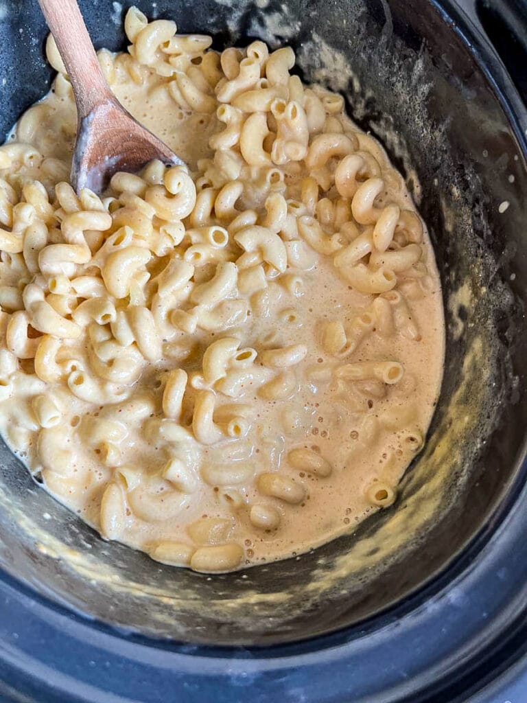 a slow cooker filled with macaroni cheese and a wooden spoon.