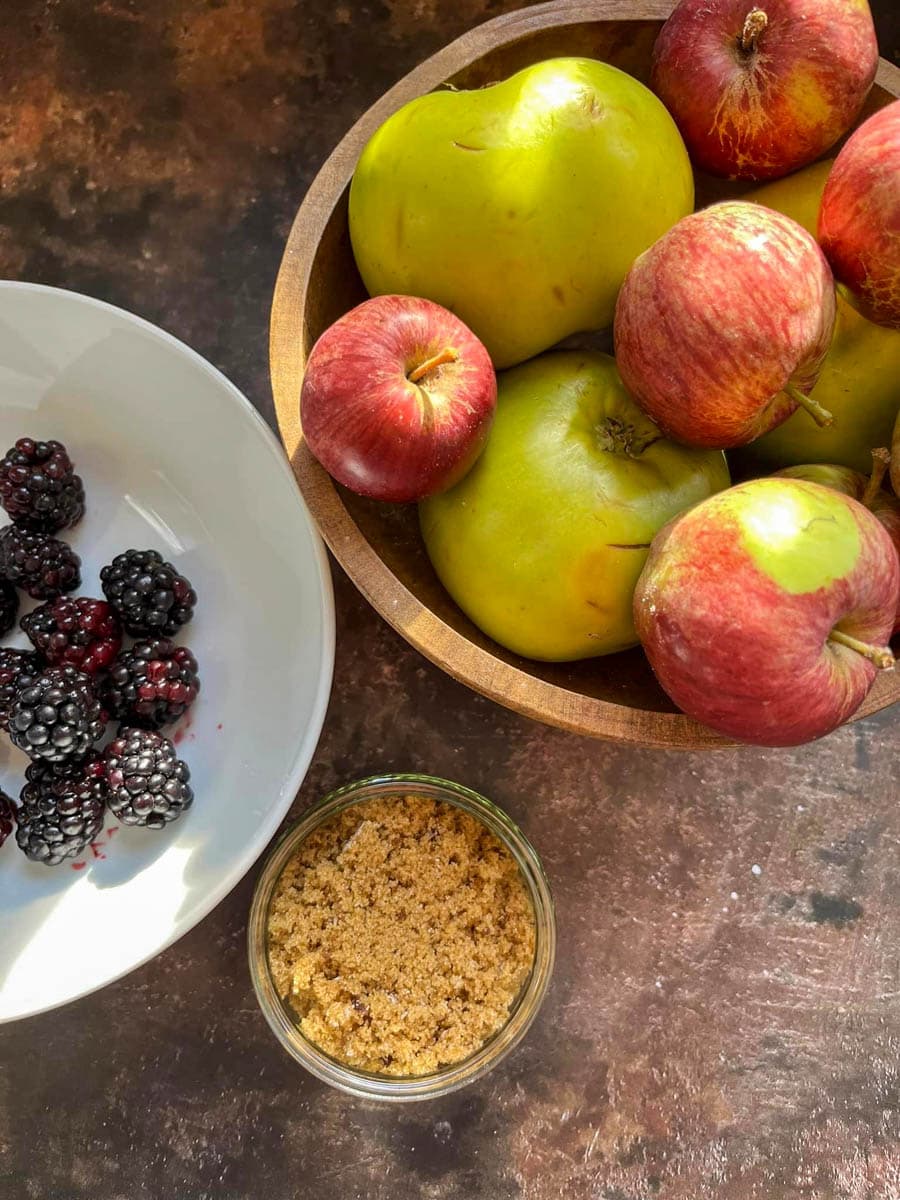a wooden bowl of apples, a white bowl of blackberries and a small glass bowl of brown sugar.