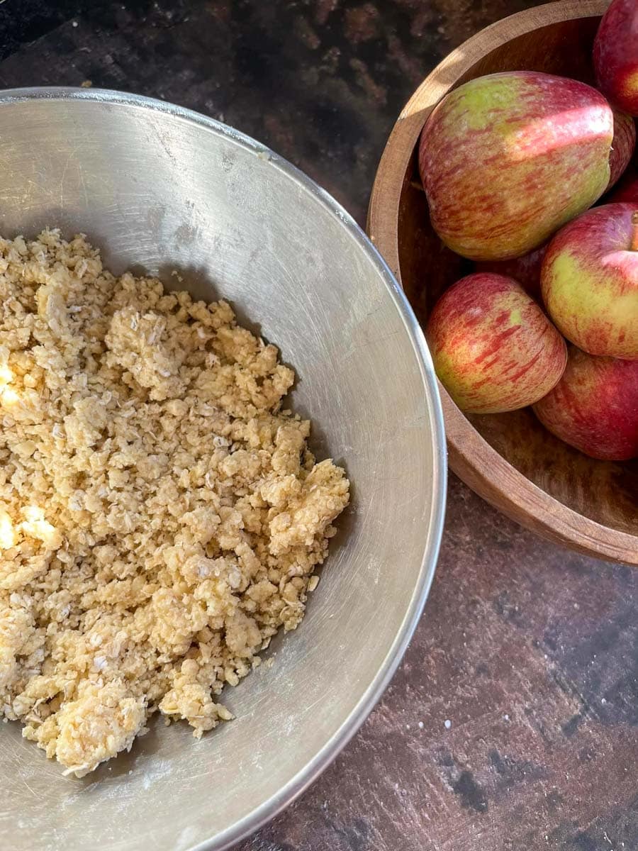 a wooden bowl of apples and a silver bowl of brown sugar.
