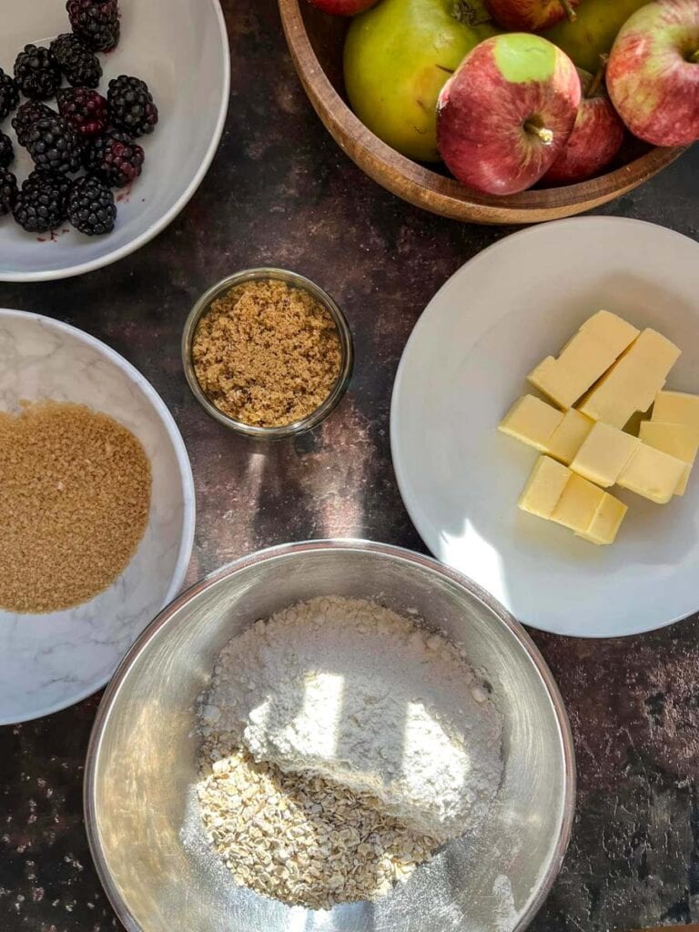 various bowls of flour, oats, brown sugar, apples and blackberries.