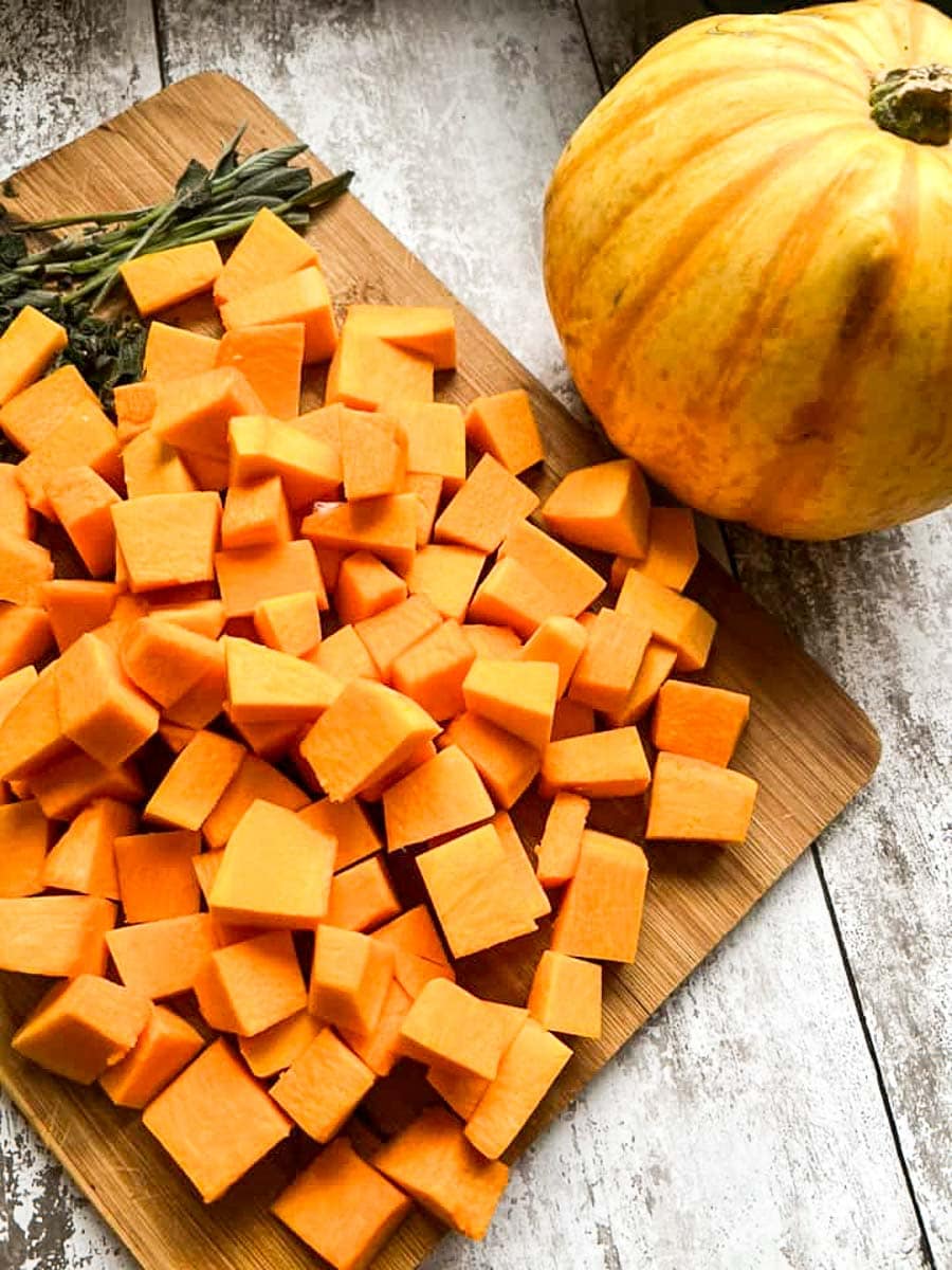 chopped pumpkin and fresh sage leaves on a wooden chopping board with a small yellow pumpkin.