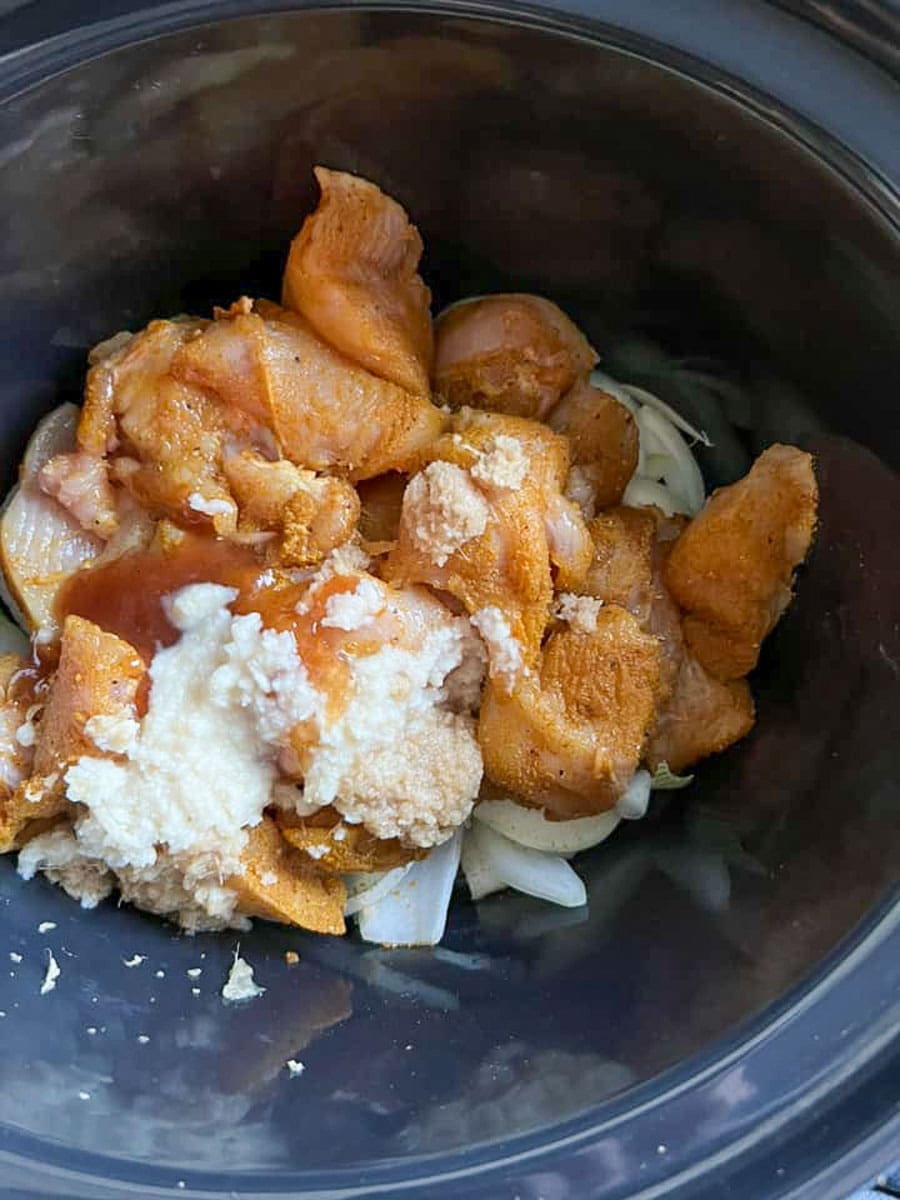 chicken strips, onion, ginger and spices inside a slow cooker pot.