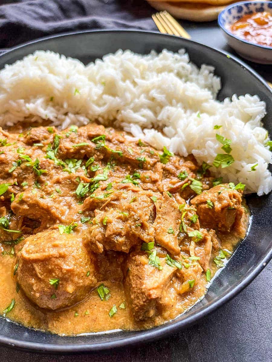 a black stoneware bowl of chicken curry with rice.