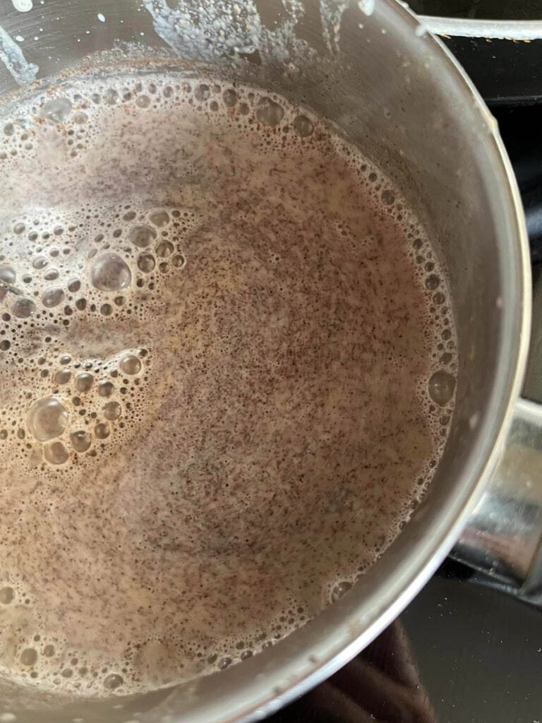 A saucepan of milk, pumpkin purée and spices heating on a stove.