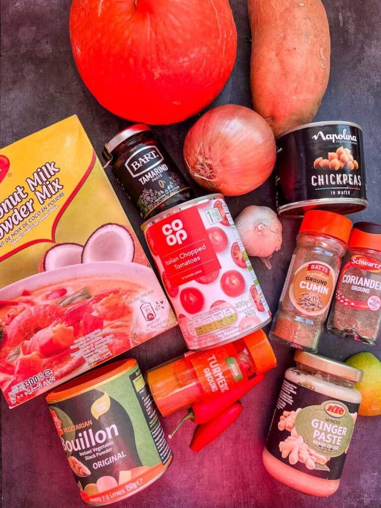 A small orange pumpkin, a sweet potato, an onion, a bulb of garlic, a box of coconut milk powder, a tub of vegetable stock, a tin of chopped tomatoes, red chillies and various jars of spices to make curry.