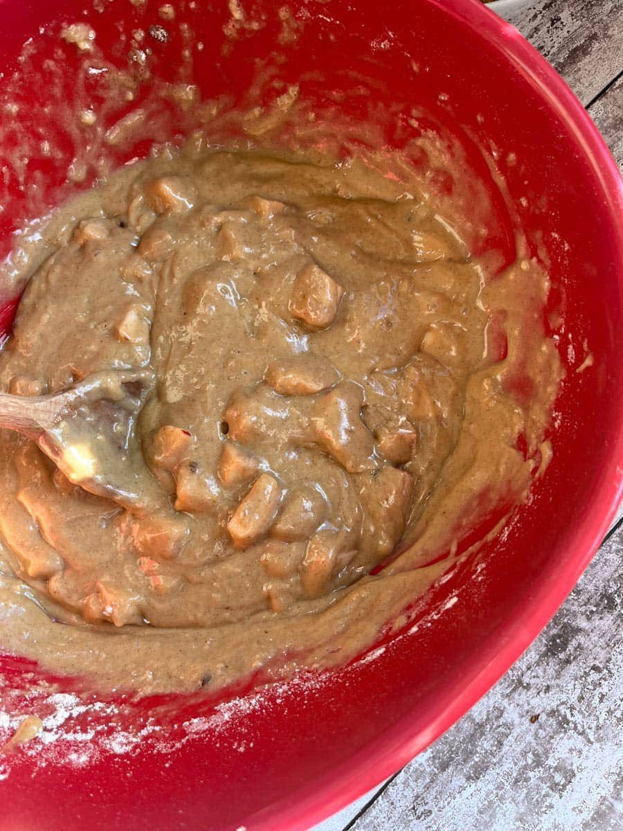 a red bowl filled with apple muffin batter and a wooden spoon.