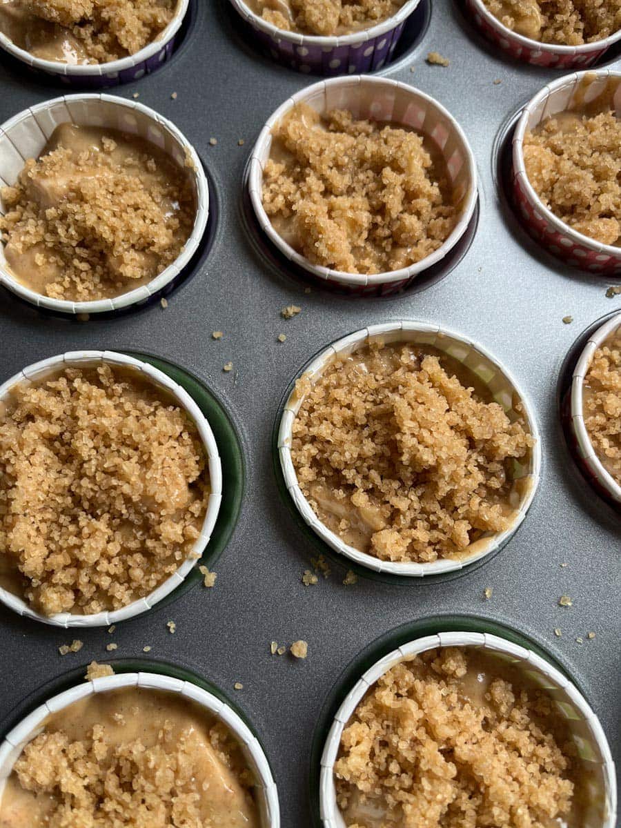 a muffin tray of unbaked apple muffins topped with a streusel crumble.