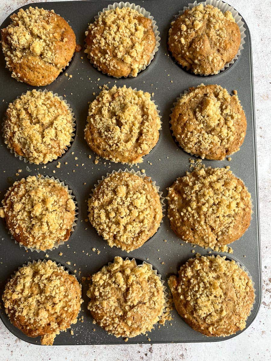 a silver muffin tray with twelve apple muffins with a streusel topping.