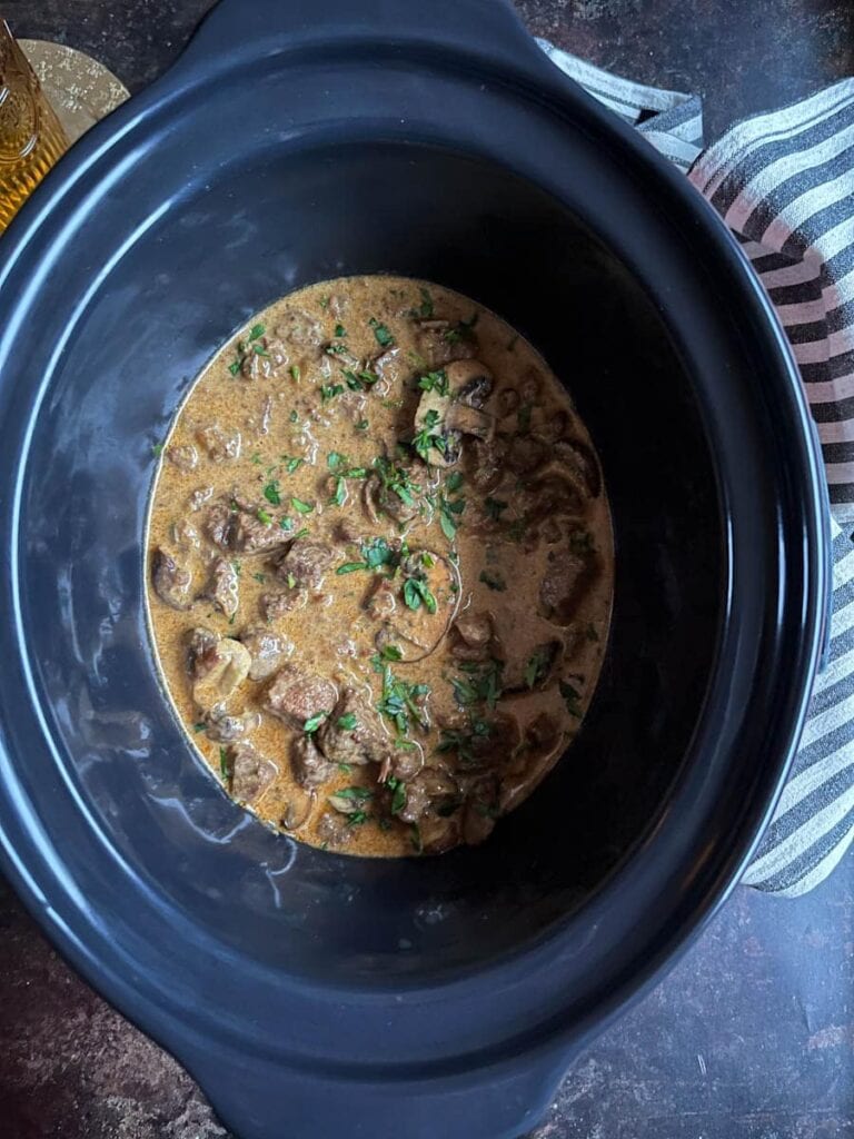 a slow cooker pot of beef and mushroom Stroganoff spinkled with freshly chopped parsley.