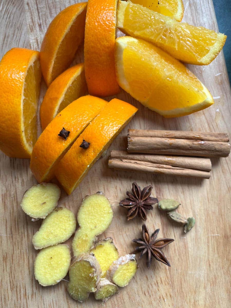 orange slices, cinnamon sticks, fresh ginger slices, two star anise and three cardamom pods on a wooden board.