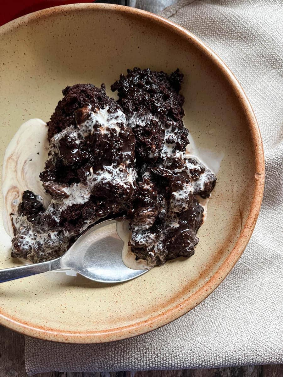 a beige stoneware bowl of chocolate pudding, cream and a silver spoon.