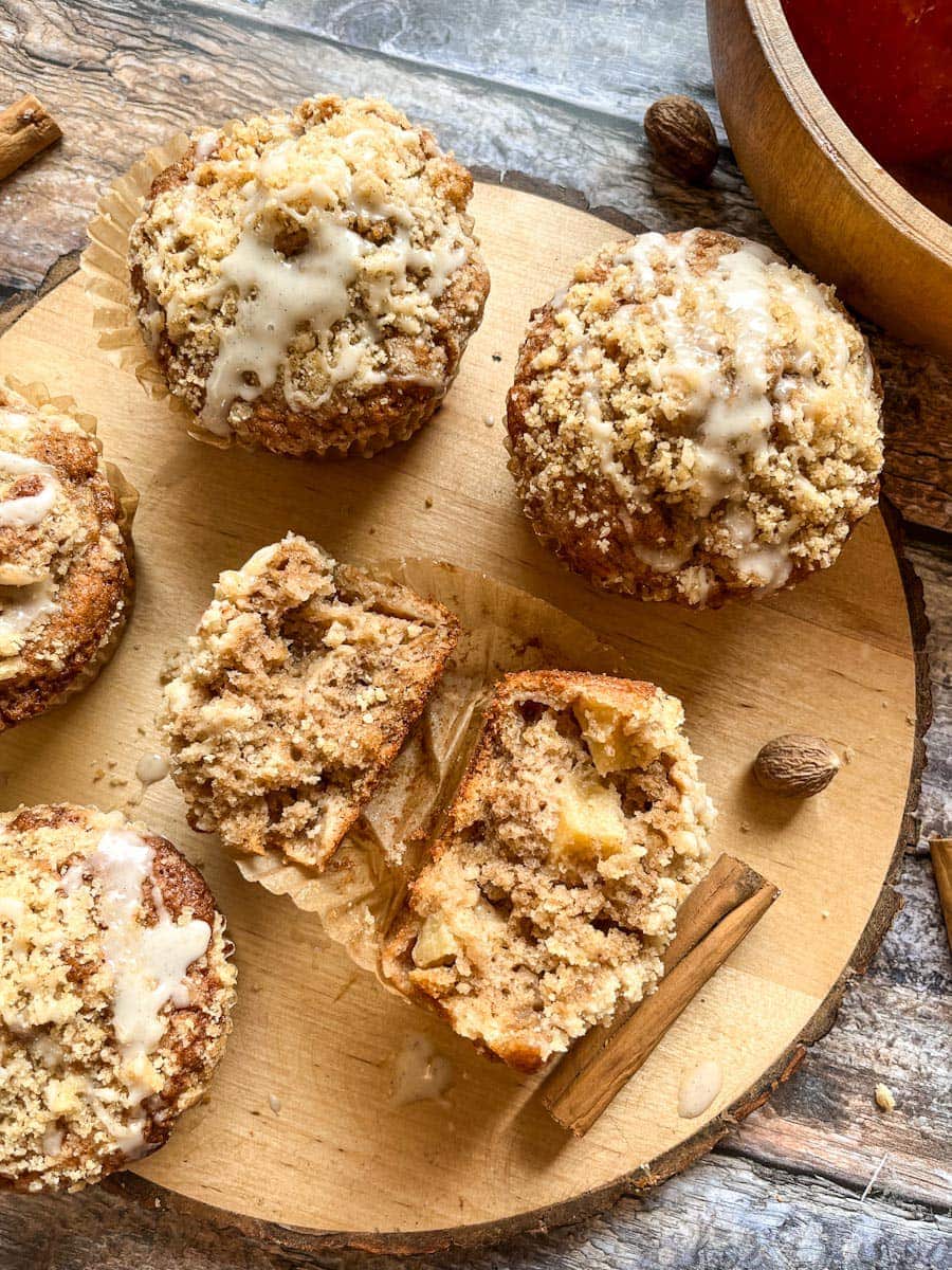 five apple muffins topped with crumble and glace icing on a wooden board. 