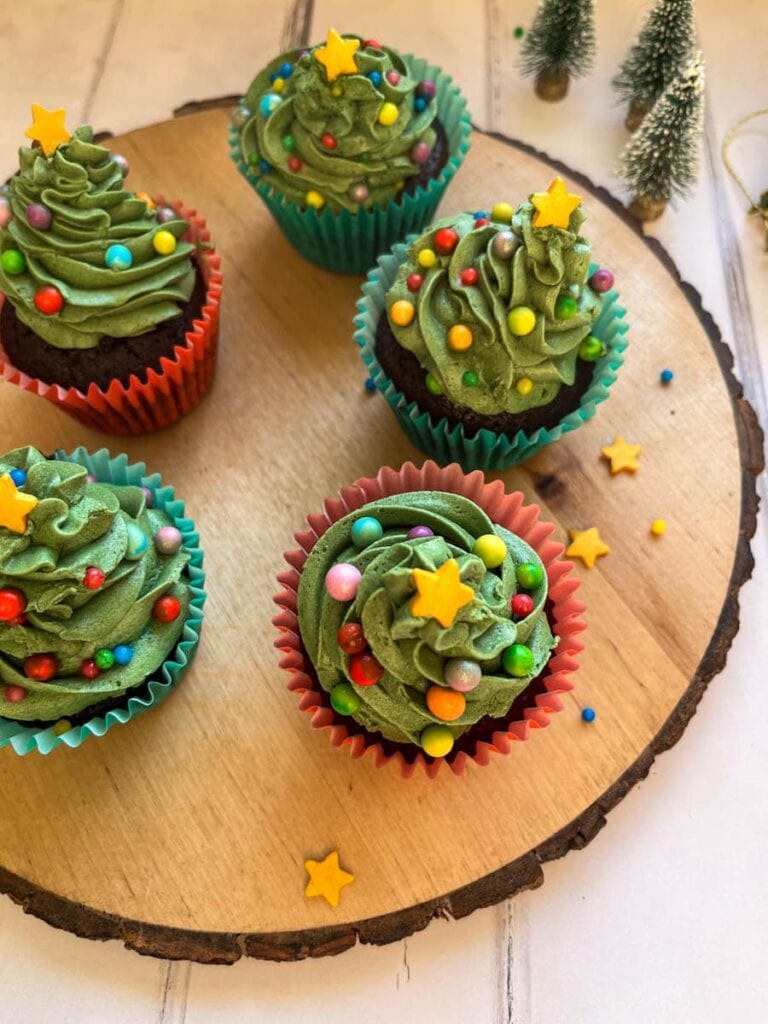 Chocolate cupcakes decorated with green buttercream icing coloured sprinkles and a gold star to resemble a Christmas tree on a wooden serving board.