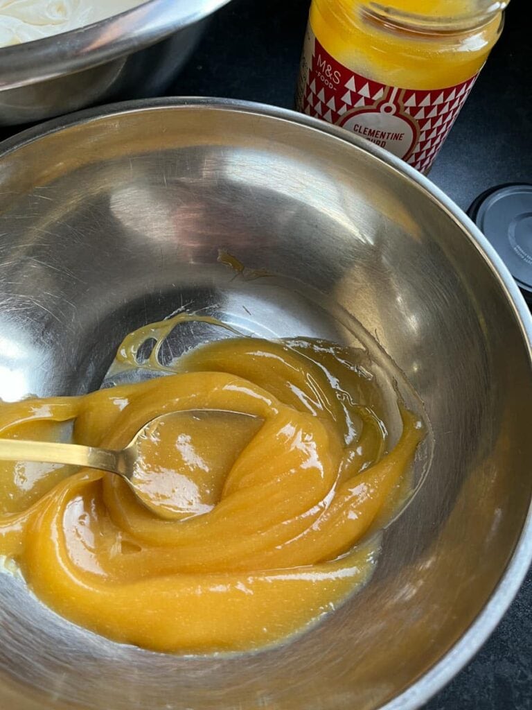 a silver bowl of orange curd with a spoon.