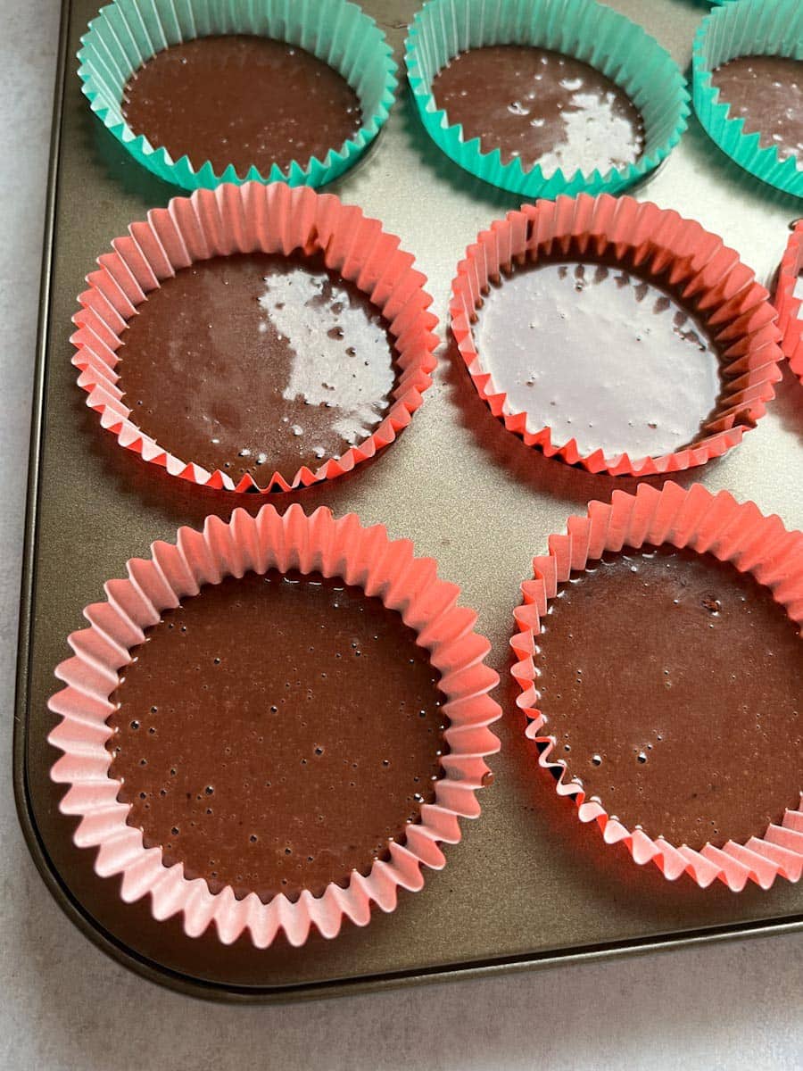 chocolate cupcake batter poured into red and green cupcake cases in a cupcake tin.